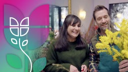 Daniel Aßmann bindet mit einer Floristin einen gelben Blumenstrauß