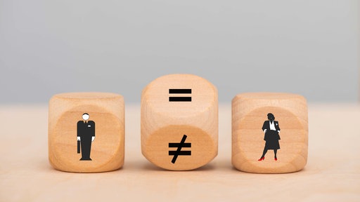 Symbolbild: Zwischen einem Würfel mit einer Figur im Anzug und einer im Kostüm liegt ein Würfel mit dem mathematischen Zeichen für 