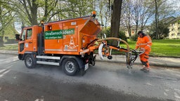 Ein oranegens kleines Fahrzeug mit einem Schlauch, das Schlaglöcher auffüllt. 