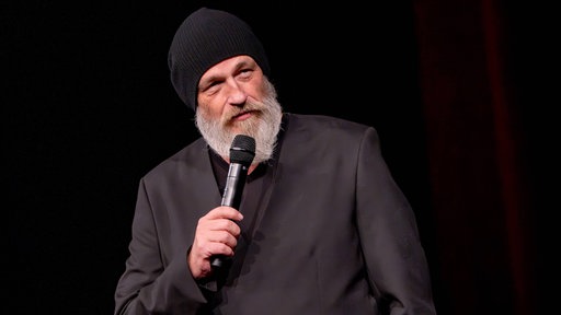 Porträt von Torsten Sträter auf einer Bühne 